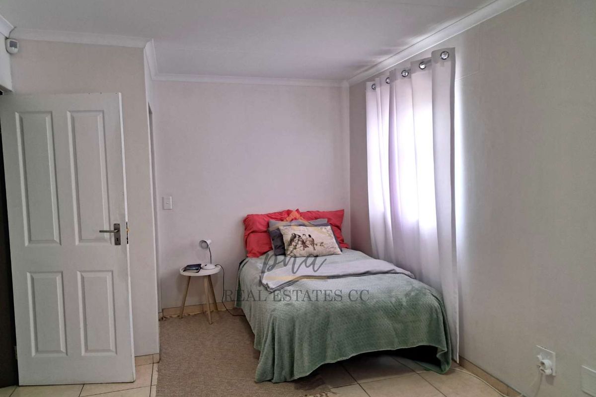 A functional bedroom featuring tiled flooring, neutral wall finishes, and a window with curtain tracks.