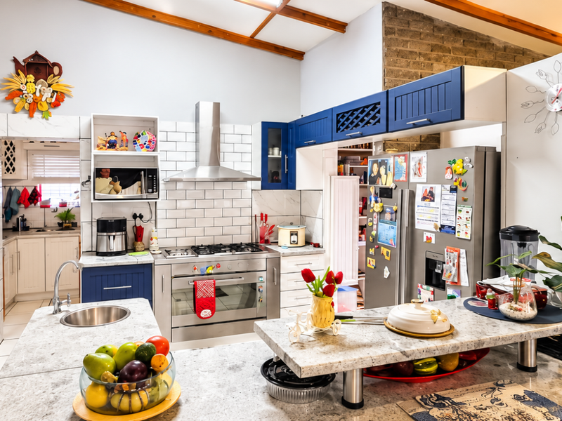 Spacious kitchen featuring a central island, subway tile backsplash, stainless steel appliances, exposed timber beams, and an adjoining scullery area.