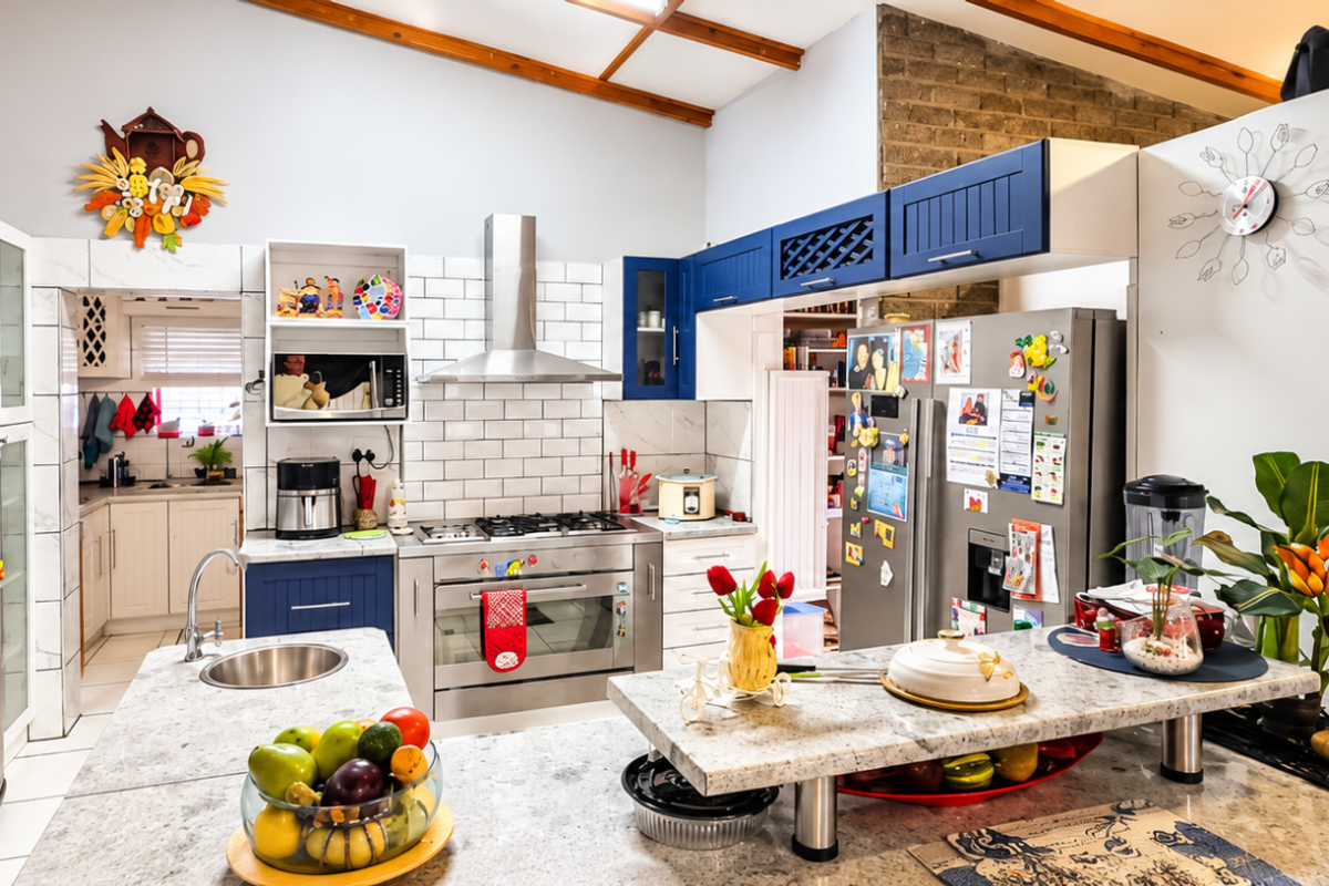 Spacious kitchen featuring a central island, subway tile backsplash, stainless steel appliances, exposed timber beams, and an adjoining scullery area.