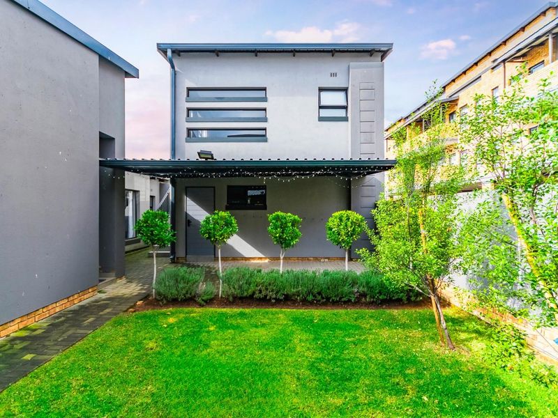 A well-maintained rear exterior view of the townhouse featuring a covered patio, paved walkway, and a neat landscaped garden.