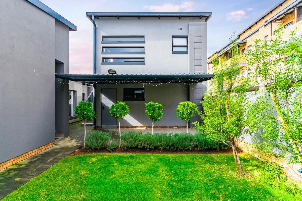 A well-maintained rear exterior view of the townhouse featuring a covered patio, paved walkway, and a neat landscaped garden.