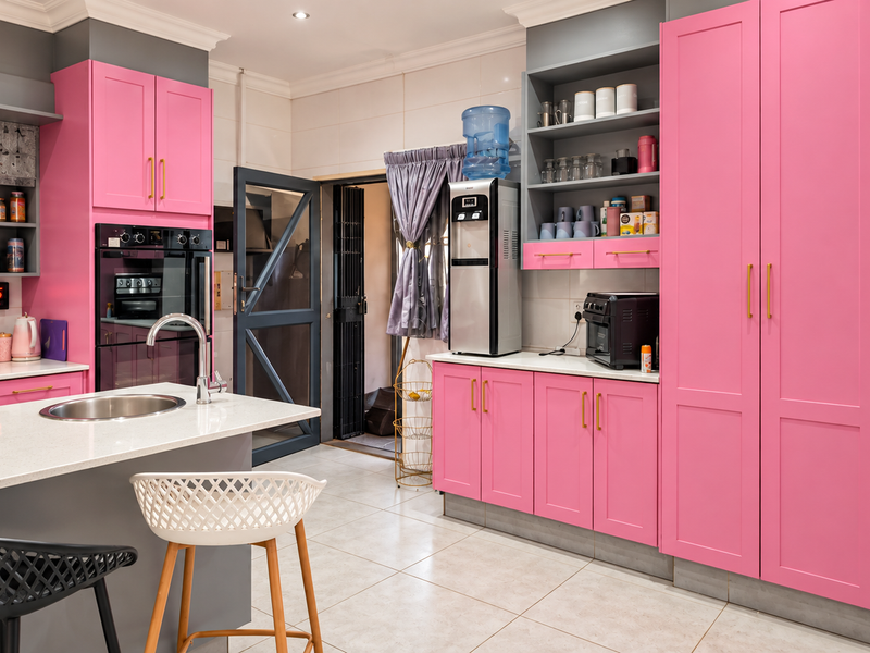 Modern kitchen featuring vibrant pink cabinetry, a central island with quartz countertops, built-in oven, and sleek tiled flooring.
