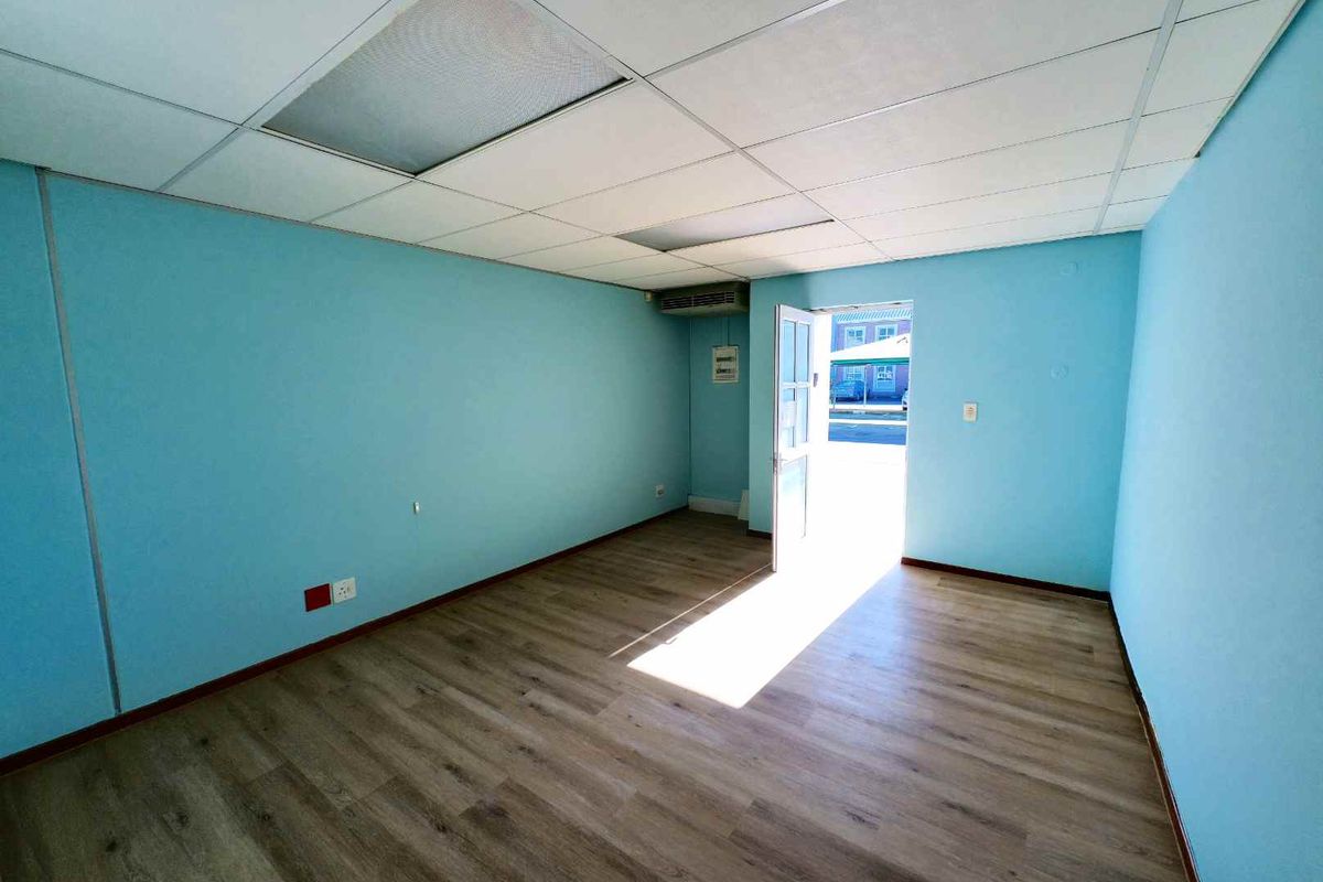 A vacant office space featuring light blue walls, wood-look laminate flooring, and a suspended ceiling with an integrated air conditioning unit.