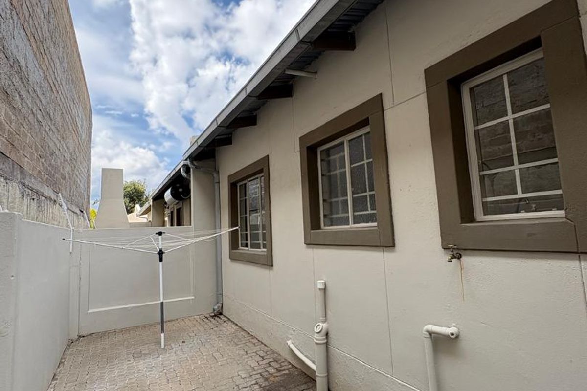 A side exterior area of the townhouse featuring paved flooring, external plumbing fixtures, and security-barred windows along the building facade.