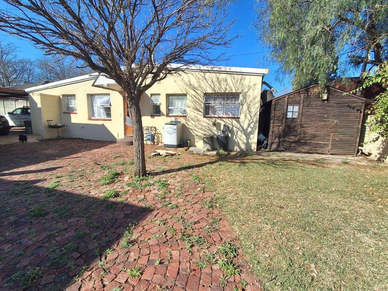 Rear exterior view of the property featuring a brick-paved yard, a detached timber storage shed, and established trees.