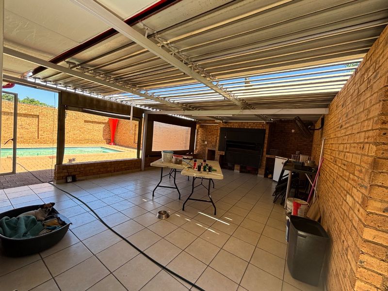 Covered outdoor patio area featuring a built-in braai, tiled flooring, and direct access to the swimming pool area.
