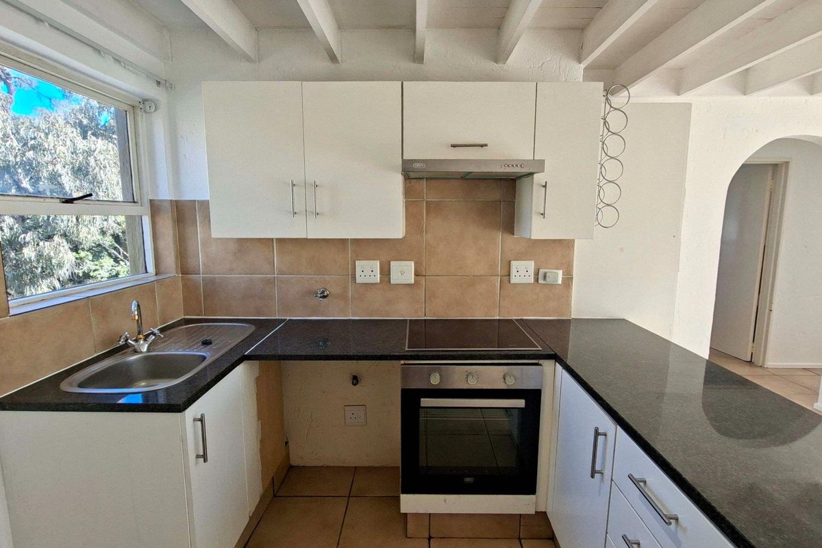 A functional kitchen featuring white cabinetry, dark granite countertops, built-in oven and hob, tiled backsplash, and exposed ceiling beams.