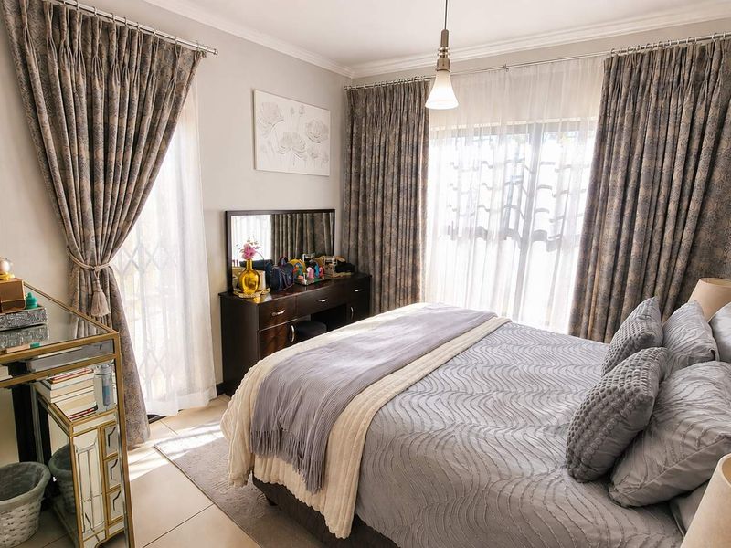 A well-maintained bedroom featuring tiled flooring, neutral walls, and large sliding glass doors with floor-to-ceiling curtains providing ample natural light.