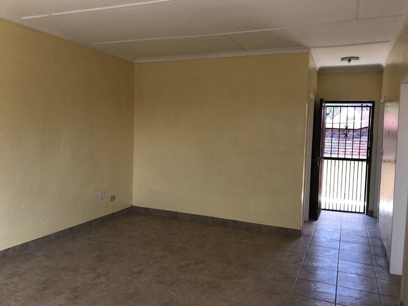 An empty living room featuring tiled flooring and a security gate entrance, providing a blank canvas for potential interior design updates.