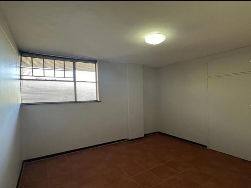 A vacant bedroom featuring tiled flooring, built-in cupboards, and a window with fitted blinds.