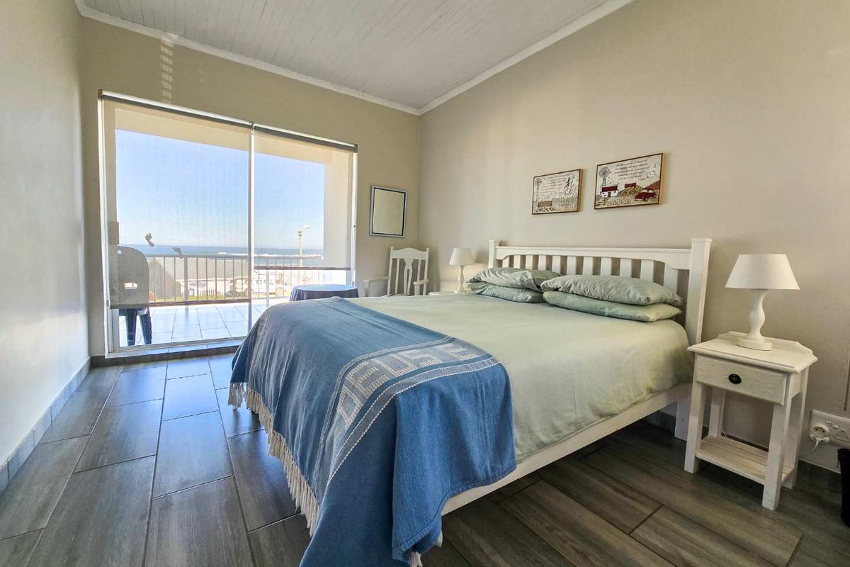 A bright bedroom featuring tiled flooring, a timber-paneled ceiling, and large sliding glass doors opening onto a balcony with ocean views.