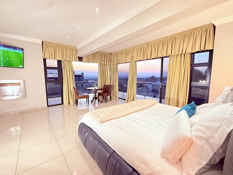 Spacious bedroom featuring large glass sliding doors leading to a balcony, tiled flooring, recessed lighting, and a built-in fireplace with scenic views.