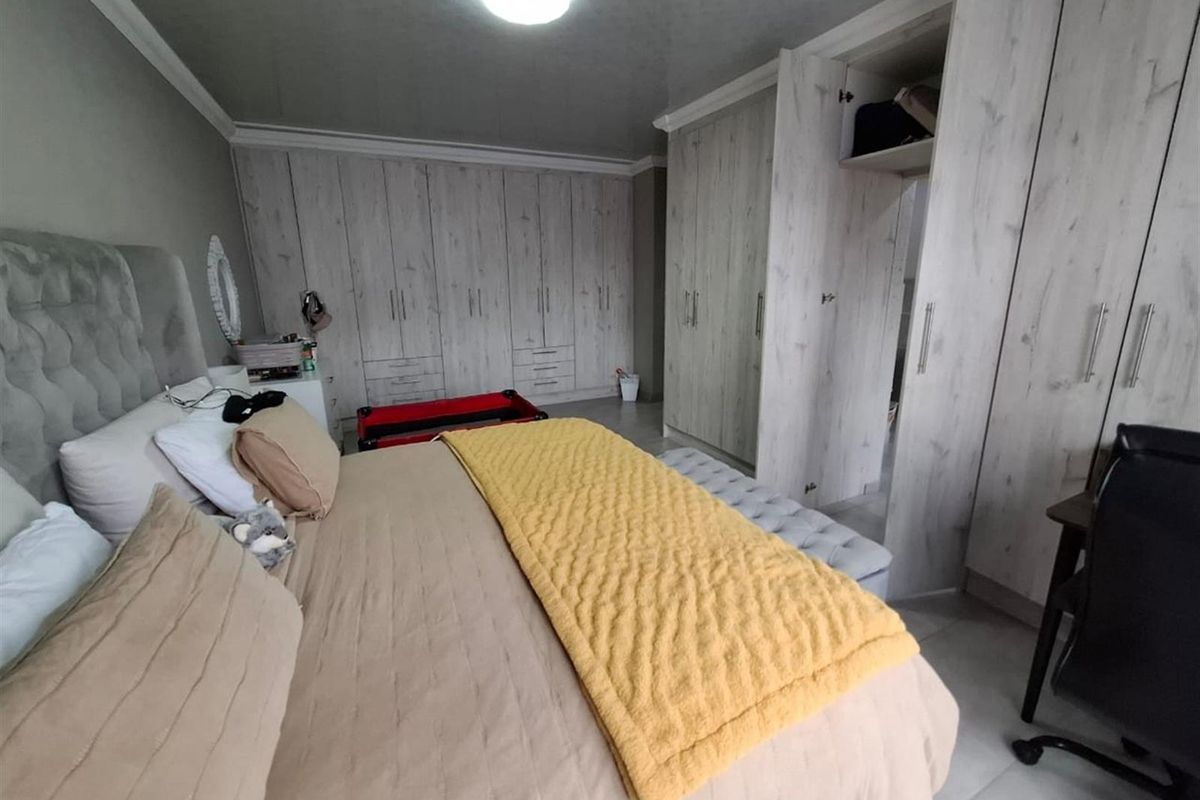 Spacious bedroom featuring extensive built-in cupboards with a light wood finish, tiled flooring, and coved ceiling detailing.