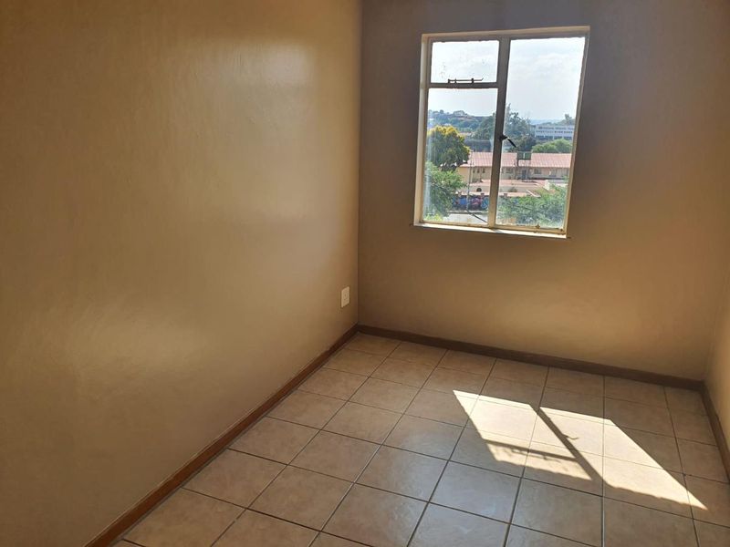 An empty bedroom featuring tiled flooring and a window with natural light, providing a blank canvas for personalization.