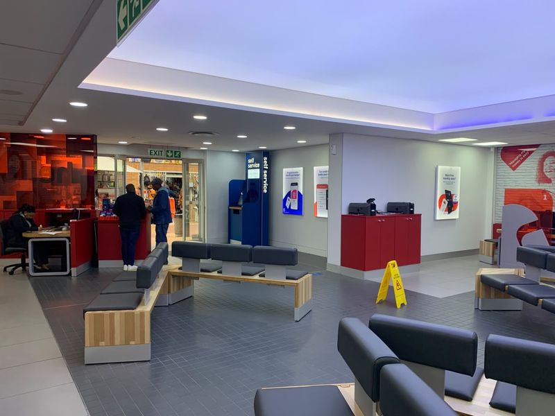 A modern, well-lit retail banking or service area featuring tiled floors, built-in service counters, and integrated seating for customers.