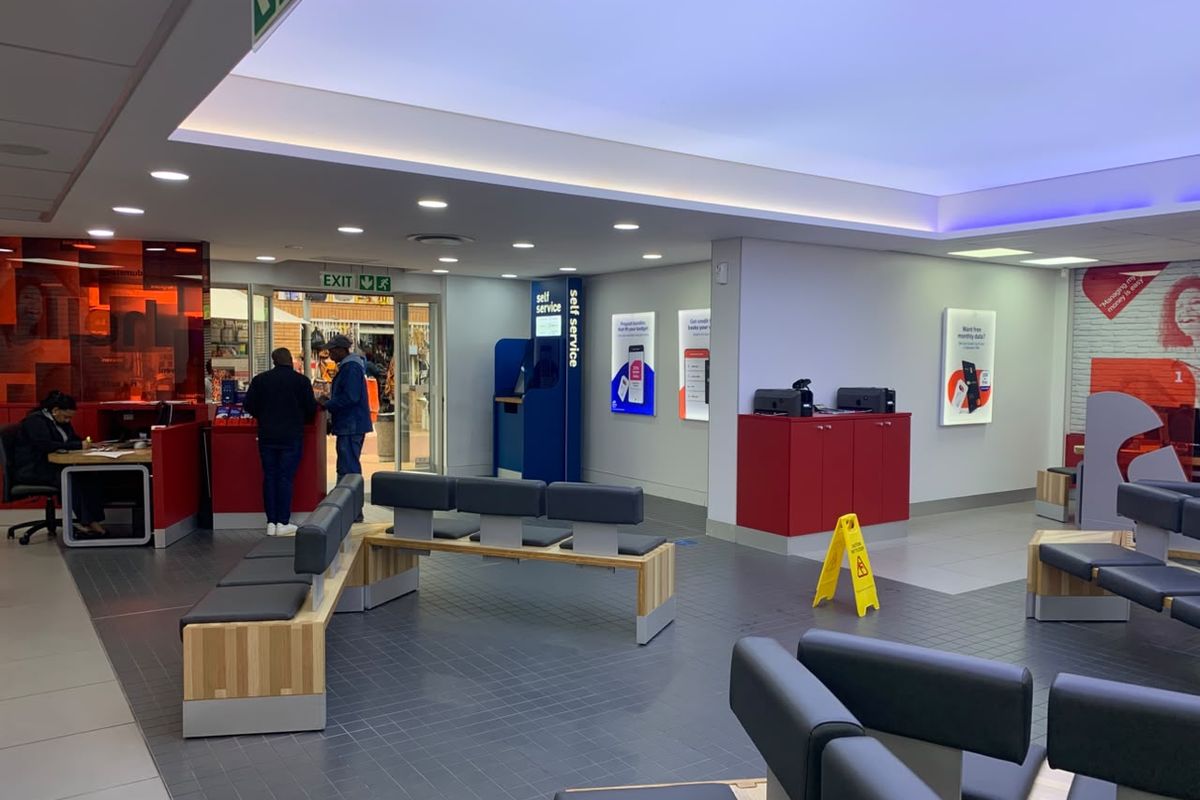 A modern, well-lit retail banking or service area featuring tiled floors, built-in service counters, and integrated seating for customers.