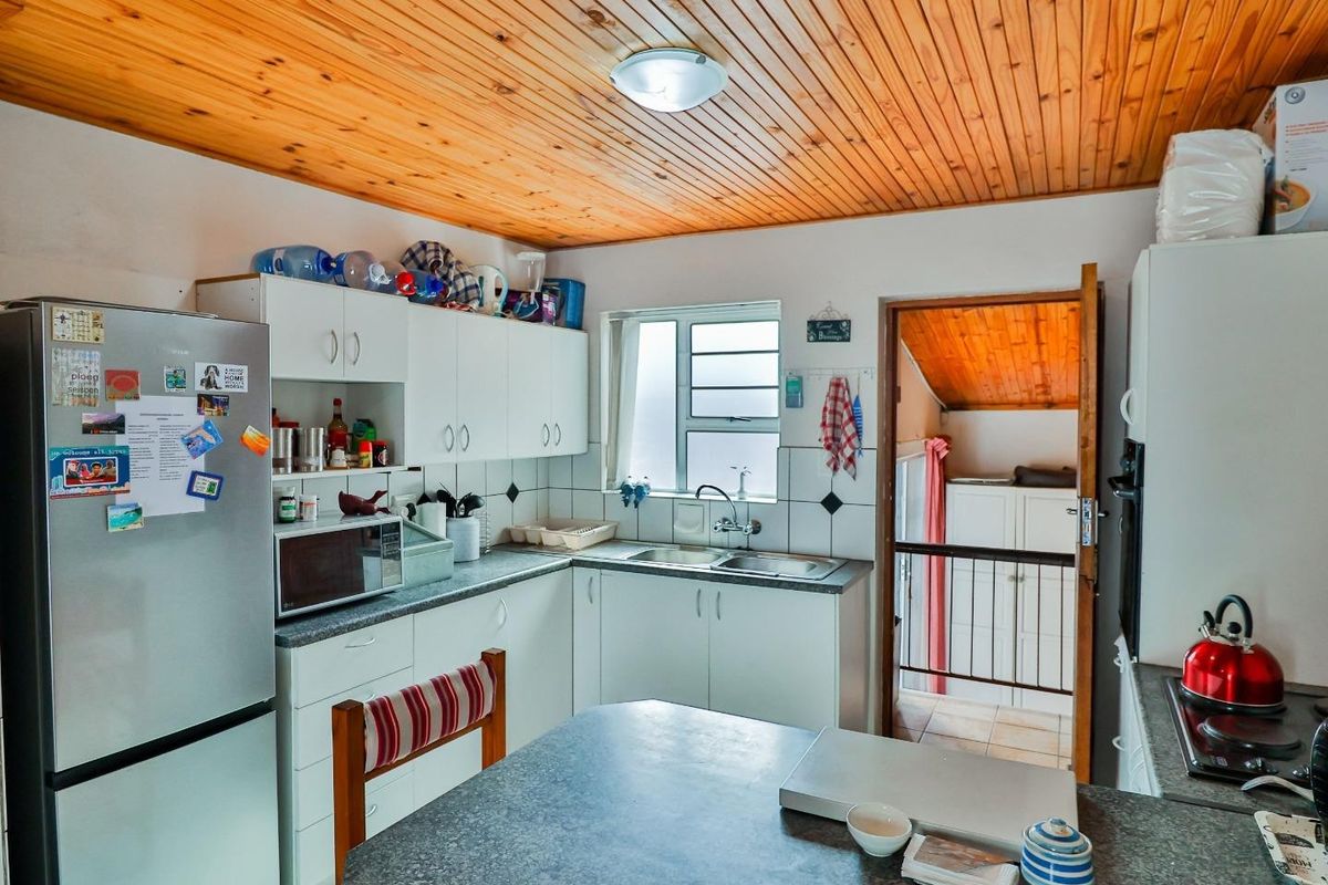 Functional kitchen featuring white cabinetry, laminate countertops, double sink, and a distinctive timber-clad ceiling, with an adjacent doorway leading to a secondary space.