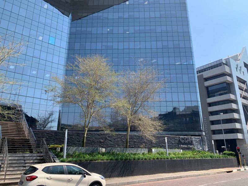 Modern commercial office building facade featuring a glass curtain wall, stone base detailing, and landscaped exterior entrance area.