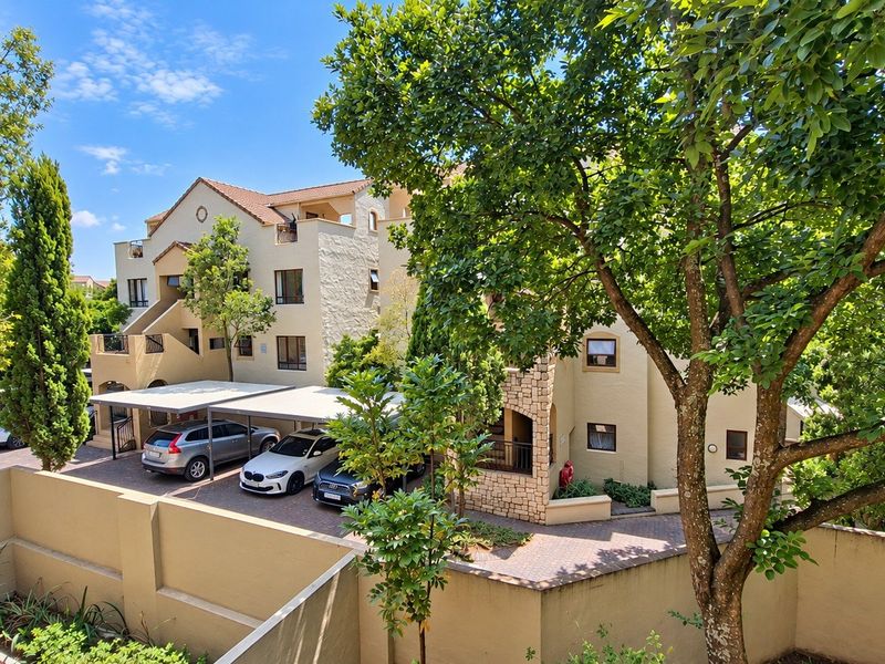 Exterior view of an apartment complex featuring a paved driveway, covered parking bays, and well-maintained building facades with tiled roofing.