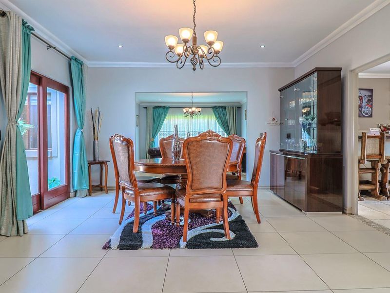 Spacious dining room featuring tiled flooring, coved cornicing, and a central chandelier, with direct access to the patio and an adjacent bar area.