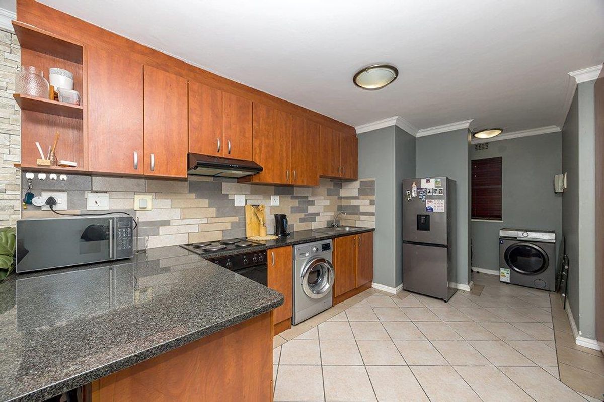 Functional kitchen featuring granite countertops, ample wooden cabinetry, integrated hob with extractor, and tiled flooring with a dedicated laundry area.