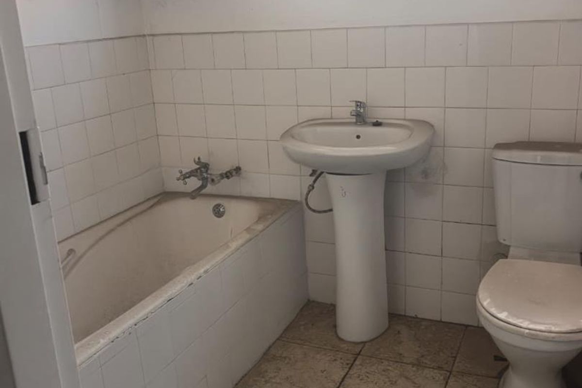 A dated bathroom featuring a standard bathtub, pedestal basin, and toilet, with tiled flooring and wall finishes requiring maintenance or renovation.