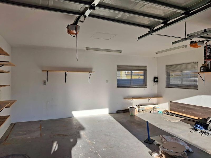 A spacious, empty garage featuring a sectional door, functional lighting, and fixed wall shelving, offering a clean slate for storage or workshop use.