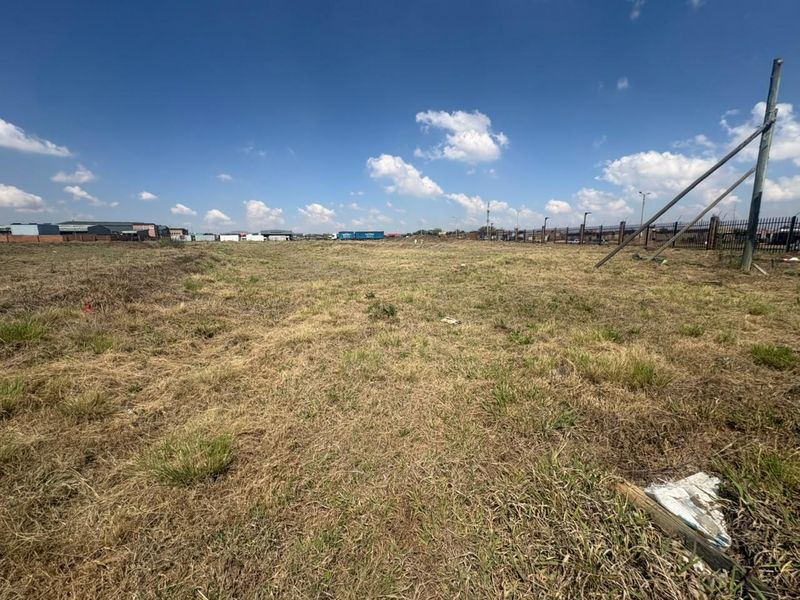 A wide-angle view of a vacant commercial land plot featuring perimeter fencing and utility infrastructure under a clear sky.