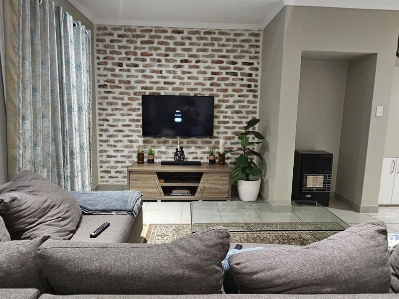 A comfortable living room featuring an exposed brick accent wall, tiled flooring, and a staircase with integrated under-stair storage cabinetry.