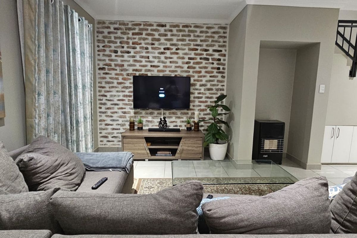 A comfortable living room featuring an exposed brick accent wall, tiled flooring, and a staircase with integrated under-stair storage cabinetry.