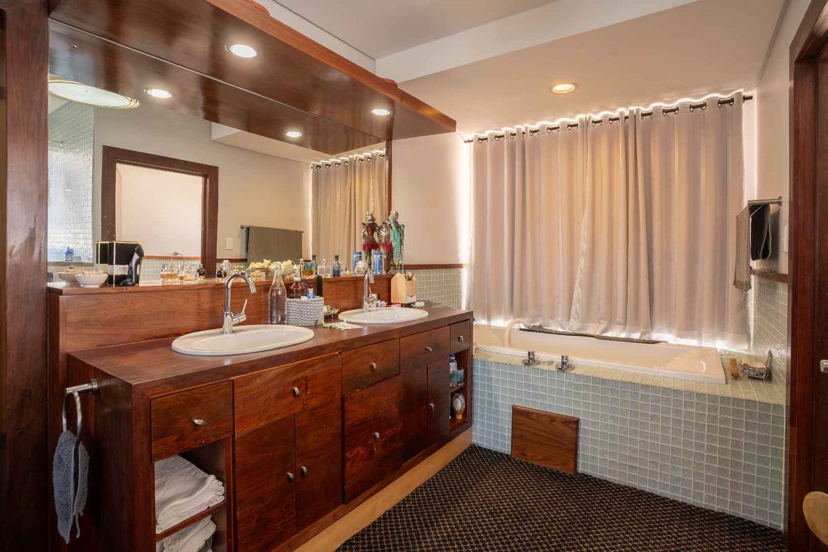 A spacious bathroom featuring a double vanity with wooden cabinetry, a large mirror, and a built-in bathtub with tiled surround.