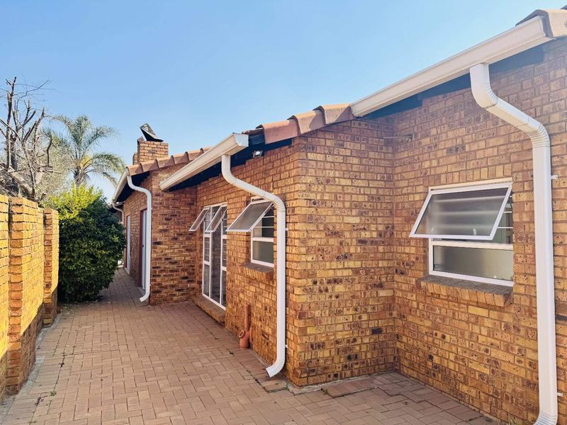 A view of the rear exterior of the cluster home, featuring face brick walls, tiled roofing, and a paved walkway along the side.