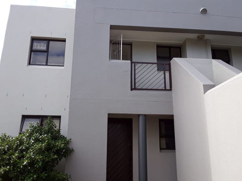 Front elevation of a modern apartment building featuring clean grey facade, aluminium window frames, and a private balcony with metal railing.