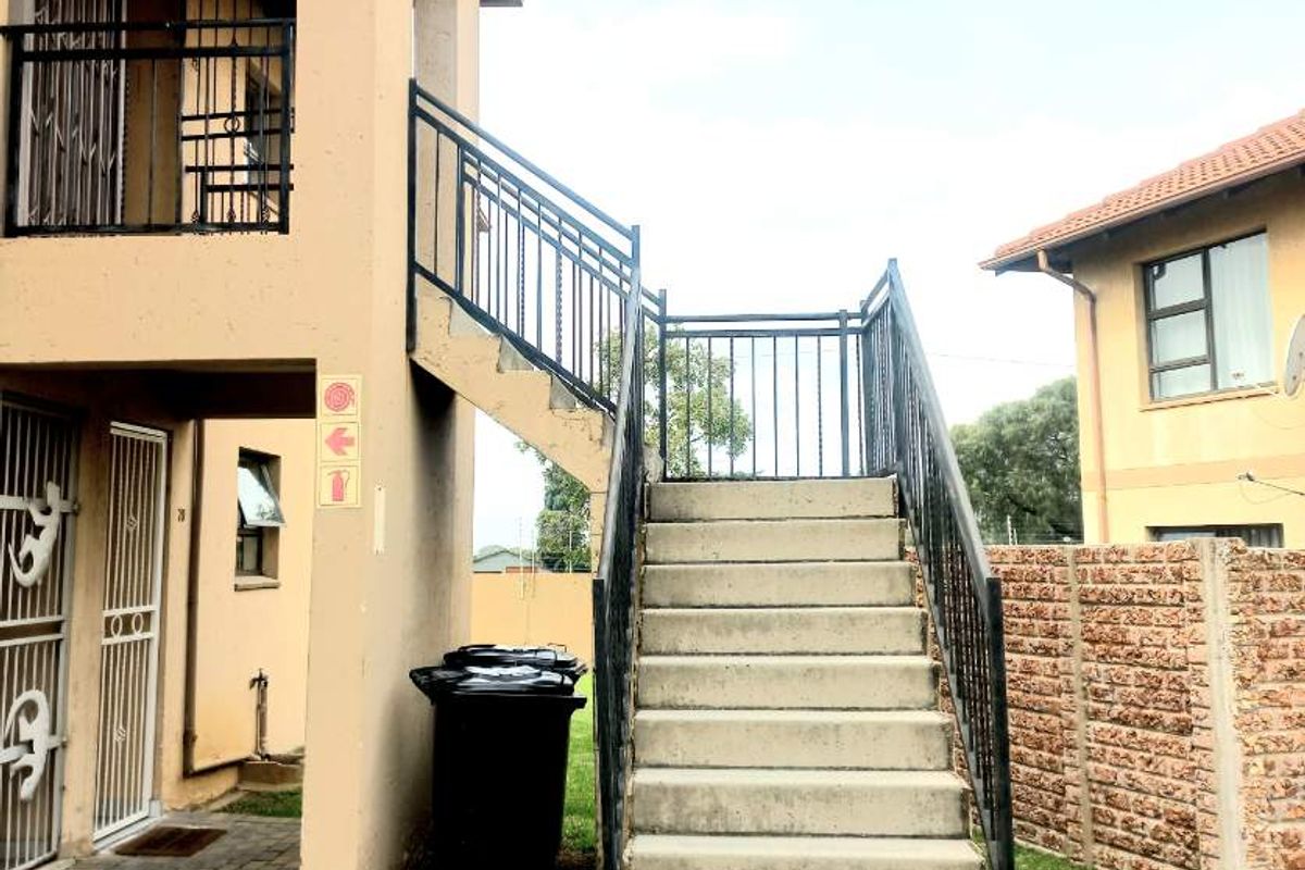 Exterior view of an apartment building featuring a concrete staircase with metal railings, paved walkway, and access to upper-level balcony.