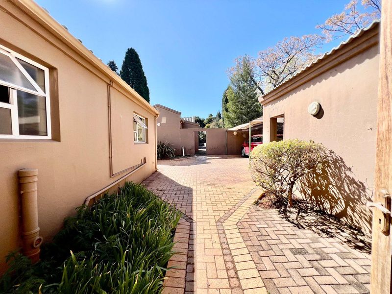 A paved driveway leading between two residential structures, featuring exterior wall lighting and well-maintained plaster finishes.