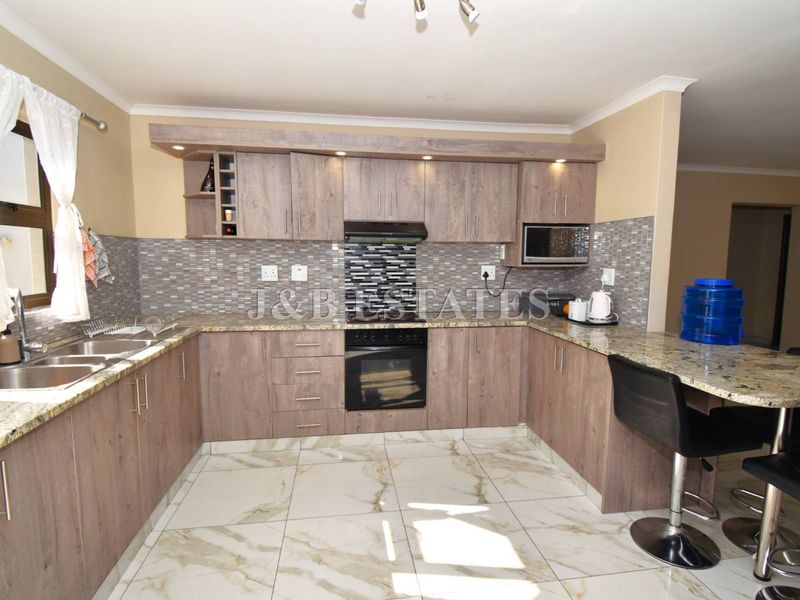 Modern kitchen featuring wood-finish cabinetry, granite countertops, a mosaic backsplash, built-in oven, extractor fan, and a convenient breakfast nook with tiled flooring.