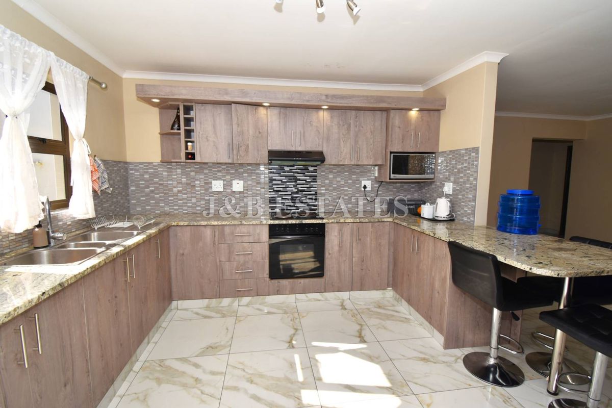Modern kitchen featuring wood-finish cabinetry, granite countertops, a mosaic backsplash, built-in oven, extractor fan, and a convenient breakfast nook with tiled flooring.