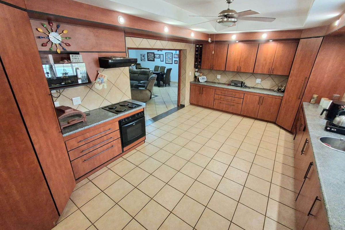 Spacious kitchen featuring extensive wooden cabinetry, tiled flooring, built-in oven and hob, and recessed lighting, with an open flow to the adjacent living area.