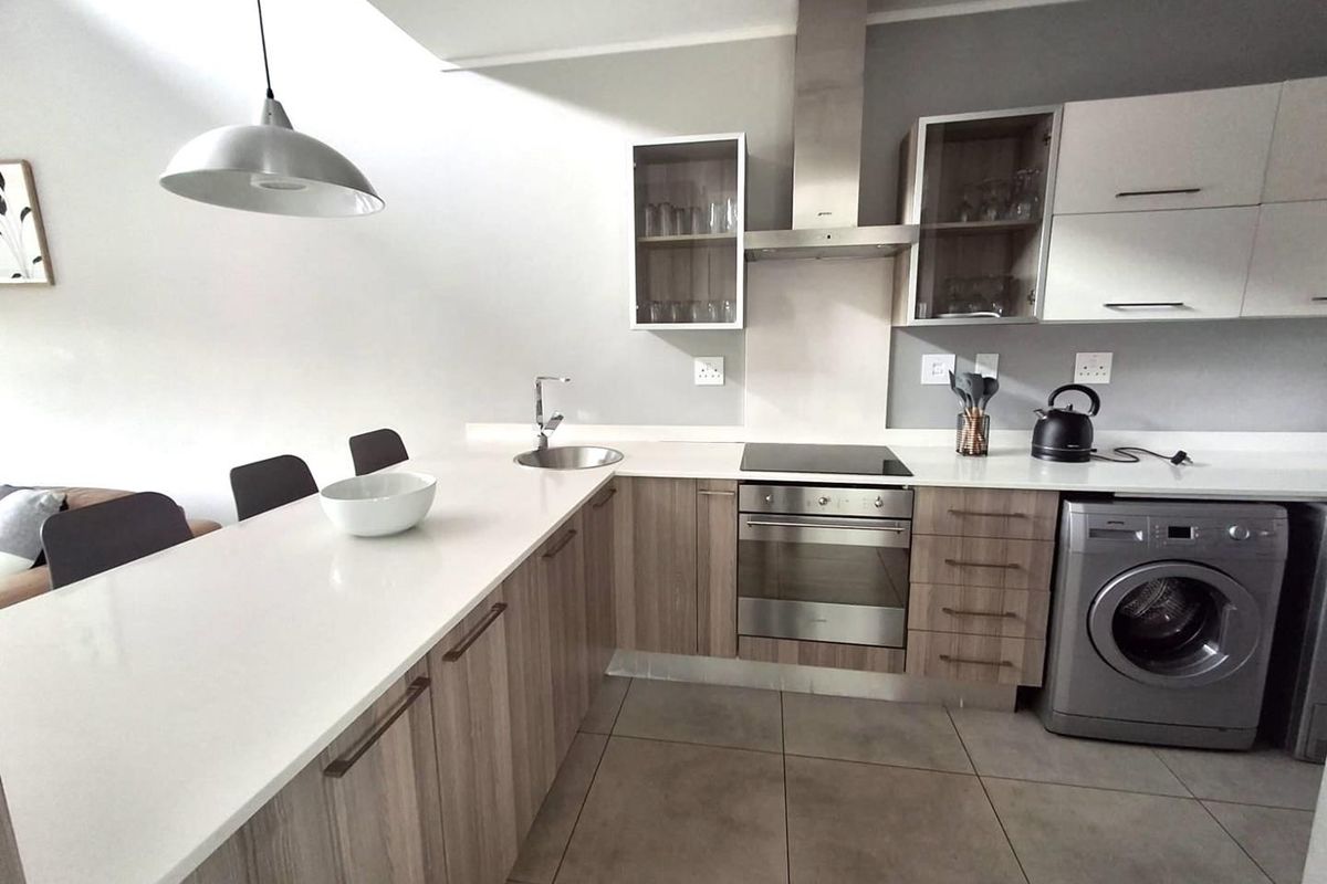 Modern kitchen featuring wood-finish cabinetry, stone countertops, integrated appliances, and a breakfast bar, complemented by neutral tiled flooring and contemporary lighting.