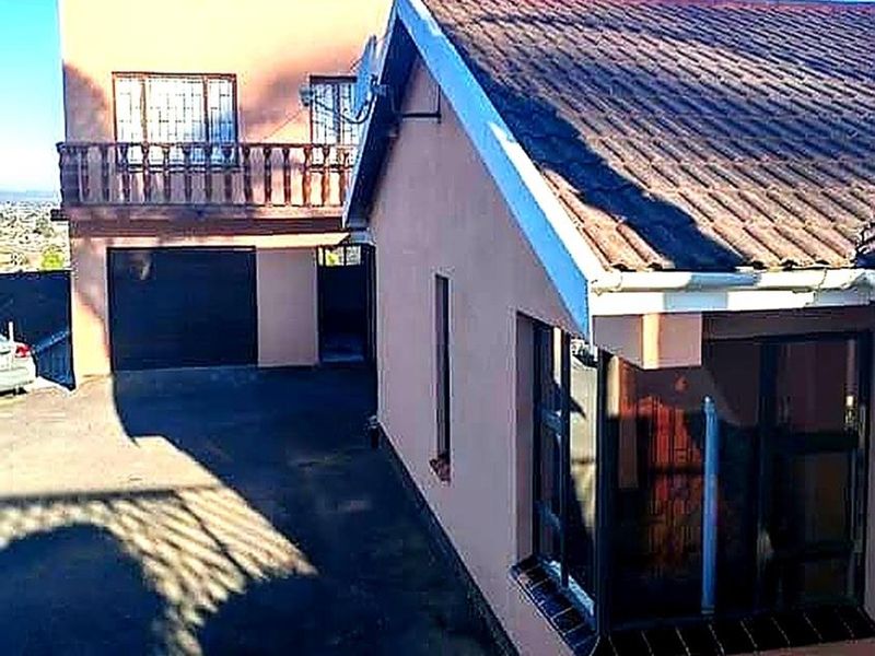 Rear view of the property featuring a tiled roof, balcony, and paved driveway area with access to the garage.