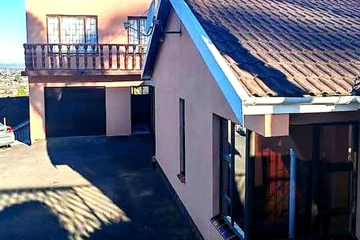 Rear view of the property featuring a tiled roof, balcony, and paved driveway area with access to the garage.