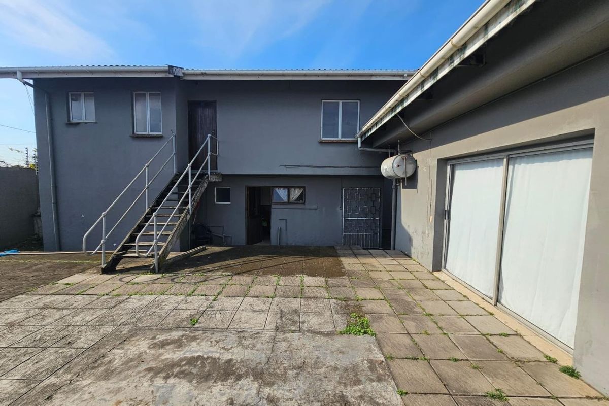 Rear exterior view of the property featuring a paved patio area, external staircase, and sliding glass doors leading into the home.