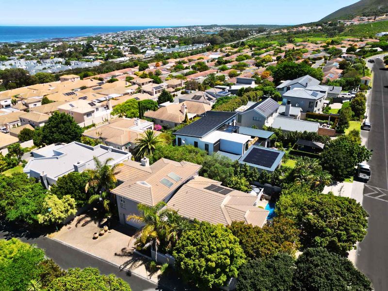 Aerial view of a residential property featuring a tiled roof with solar panels, a swimming pool, and a paved driveway in a coastal neighborhood.
