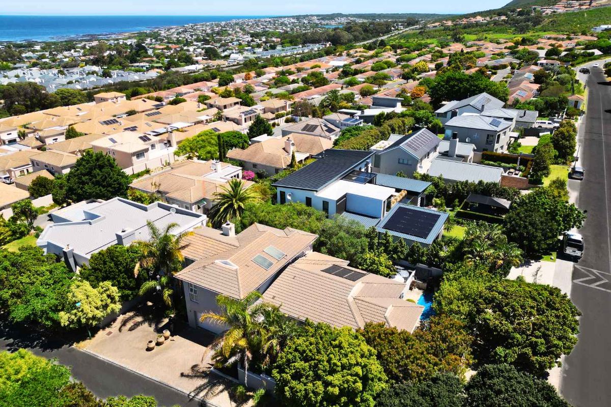 Aerial view of a residential property featuring a tiled roof with solar panels, a swimming pool, and a paved driveway in a coastal neighborhood.