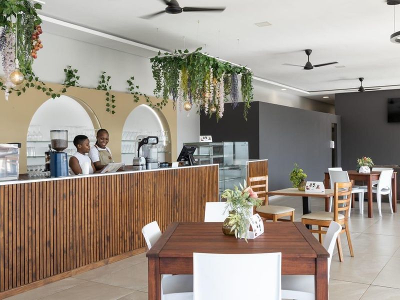 An open-plan commercial or residential space featuring a modern service counter with arched shelving, ceiling fans, and neutral tiled flooring.