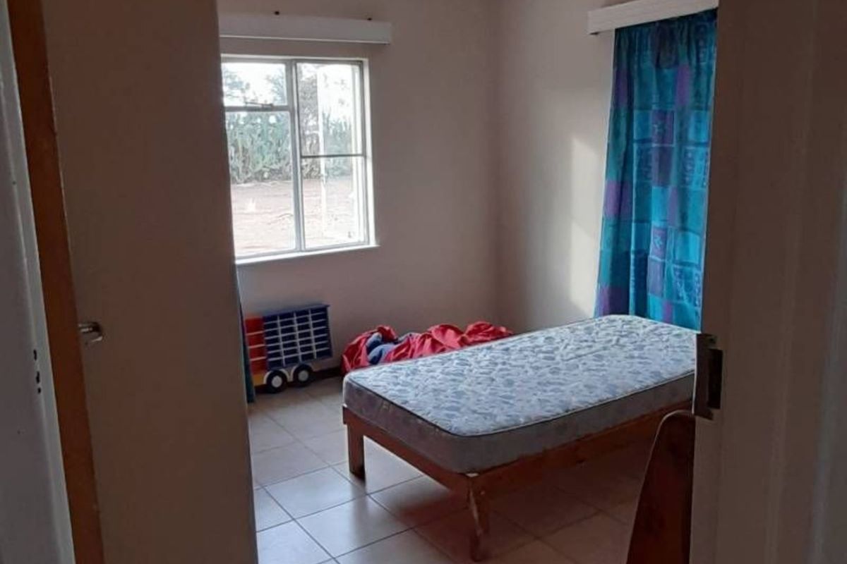 A simple bedroom featuring tiled flooring and a window with natural light, viewed from the doorway.