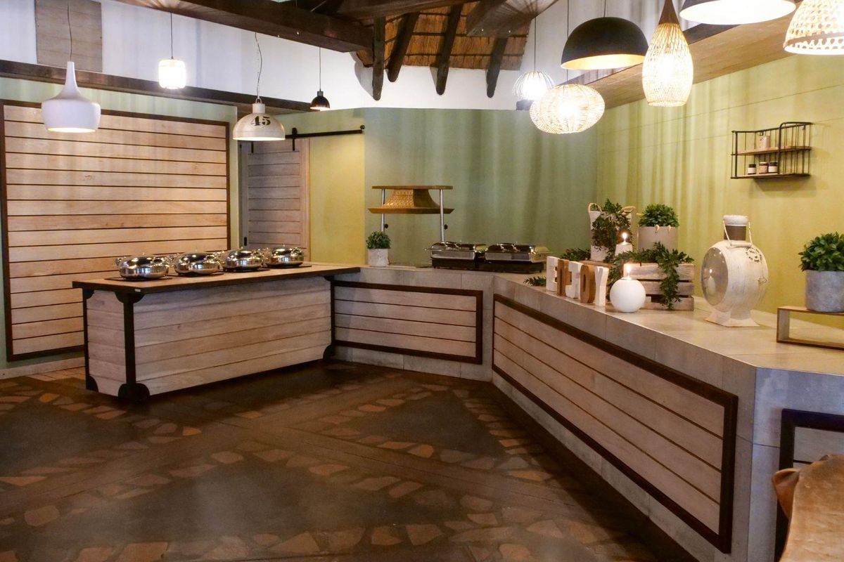 A rustic lodge-style buffet serving area featuring custom timber-clad counters, exposed timber ceiling beams, and decorative stone-inlay flooring.