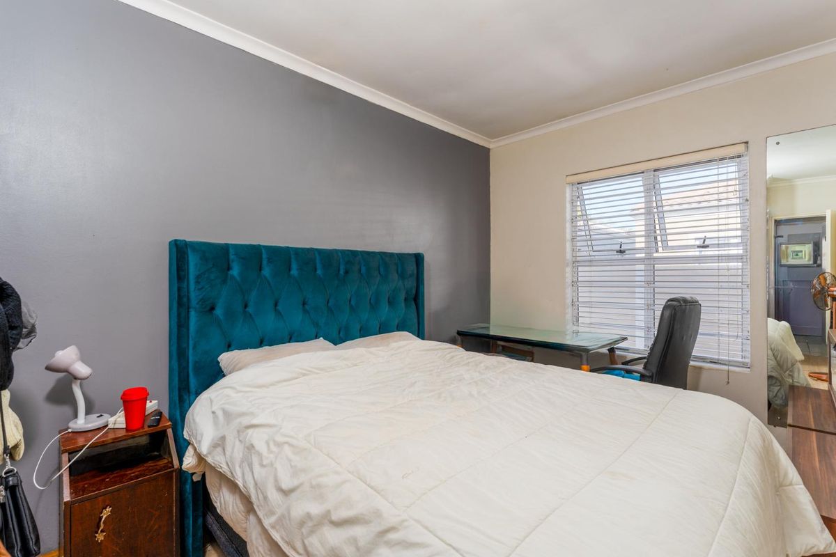 A bedroom featuring a grey accent wall, horizontal window blinds, and neutral flooring.