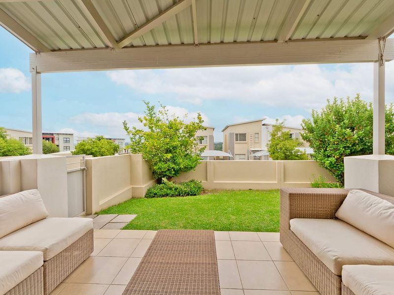 A well-maintained covered patio featuring tiled flooring and a low perimeter wall, overlooking a private garden area.