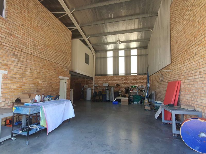 Spacious industrial utility area featuring exposed brick walls, concrete flooring, and a high-pitched metal roof with a mezzanine level.